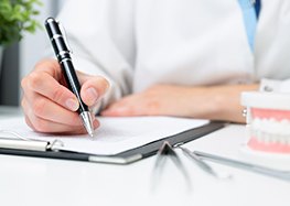 Dentist’s hand making notes during dental implant consultation