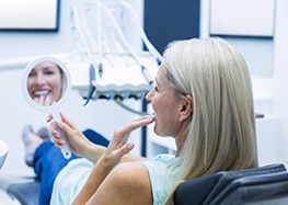 Happy dental patient admiring her new dental implant restorations in mirror