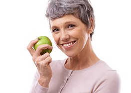 Older woman with dental implants in Rome holding an apple