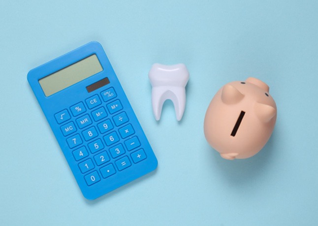 A calculator, plastic tooth, and piggy bank laying against a blue background