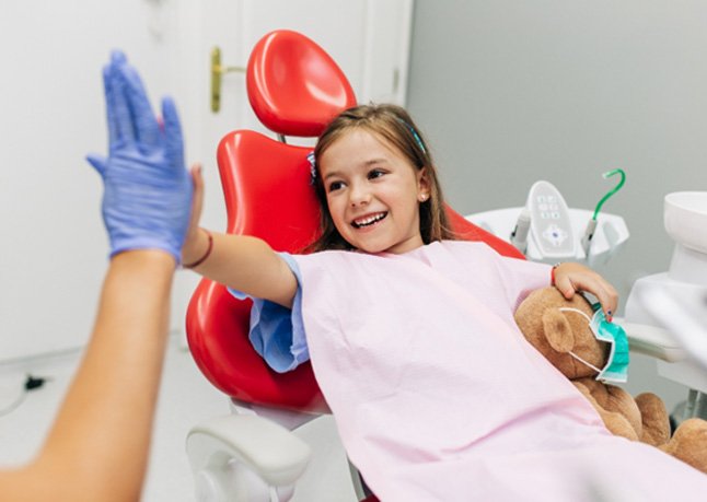 A little girl high-fiving her dentist while sitting in a chair