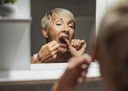 Woman flossing her teeth in bathroom mirror