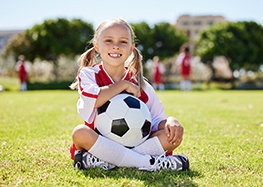 Child sits on grass with soccer ball 