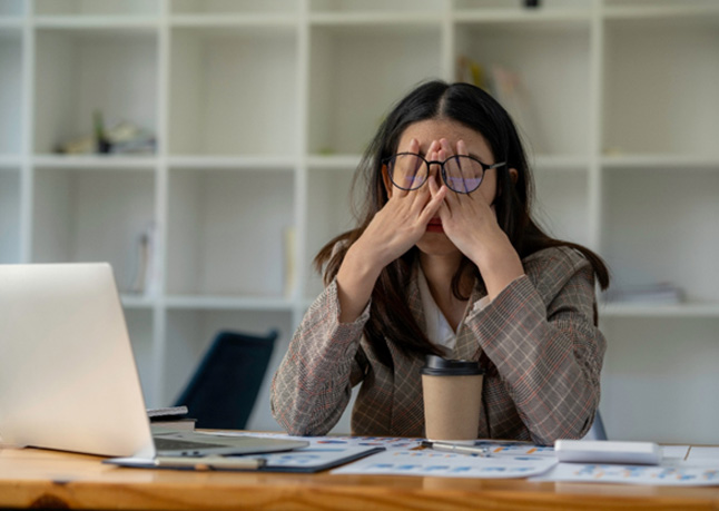 Tired woman with glasses rubbing eyes at desk