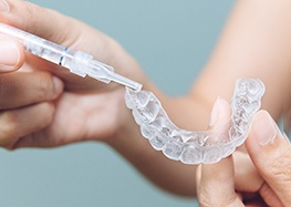 a person placing whitening gel in a customized dental tray